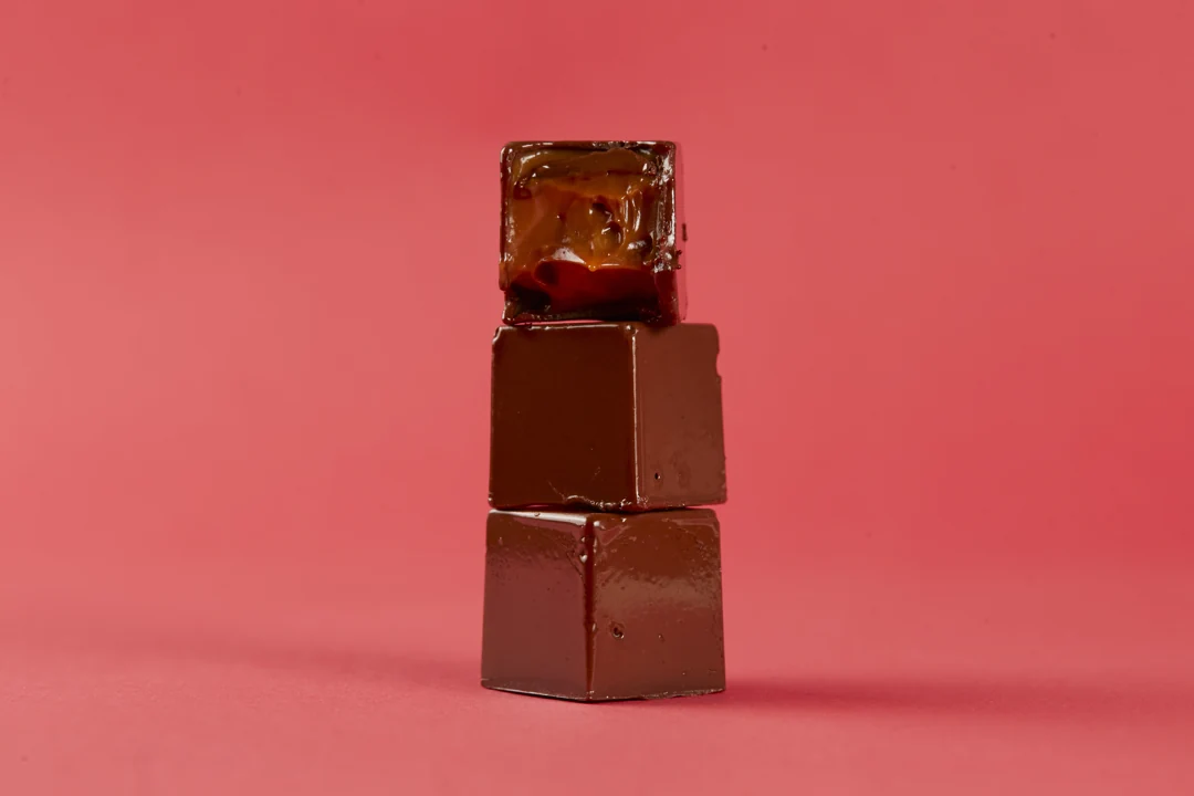 Chocolates empilhados, com recheio de caramelo à mostra, em cenário coral